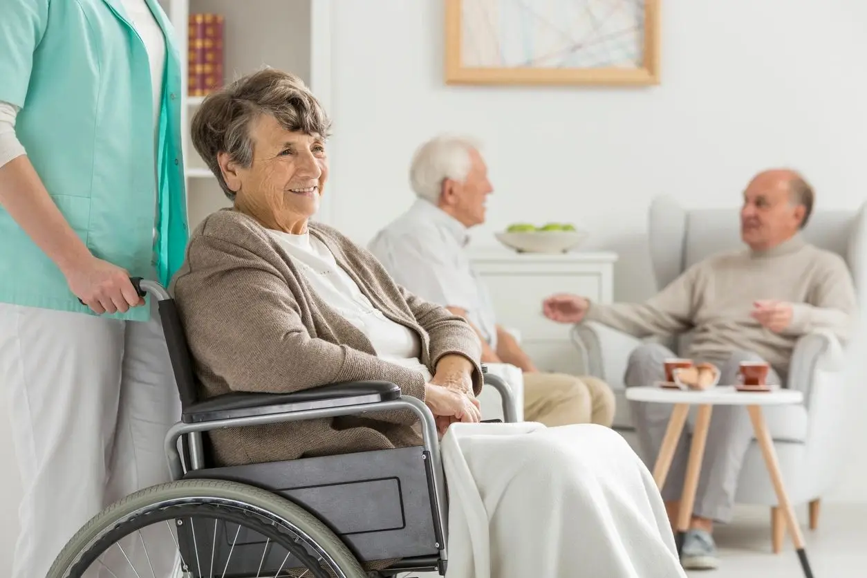 A woman in a wheelchair with two other people sitting on the couch.